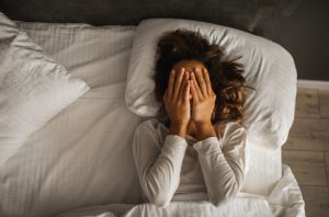 Mujer en la cama con manos tapando la cara
